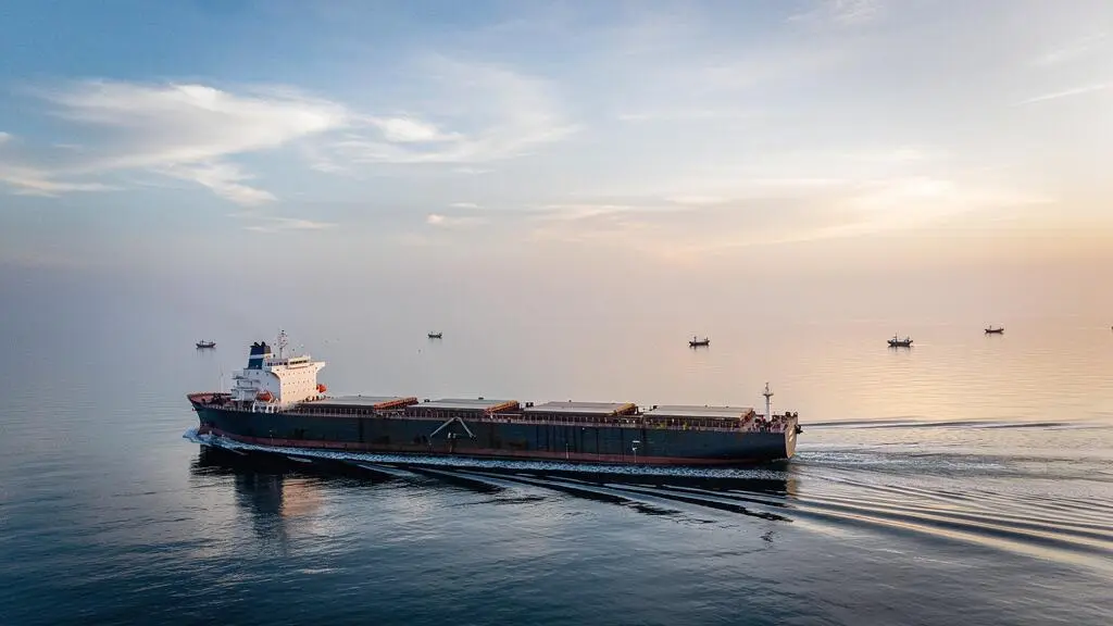 A large cargo ship moving mostly submerged beneath a calm dawn sea, symbolizing hidden institutional order flow beneath visible market surface